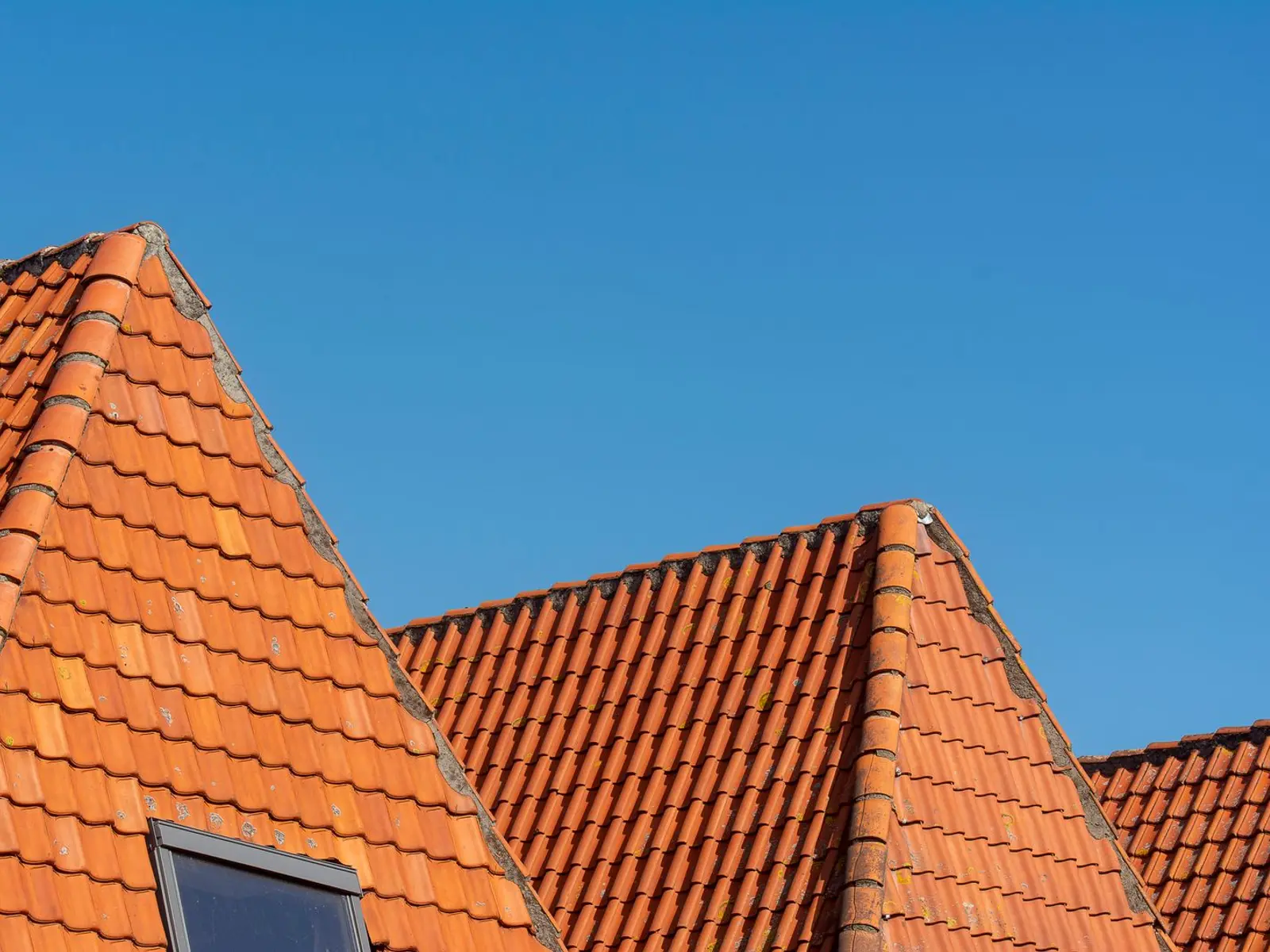 Rødt tegltag med ovenlysvindue mod blå himmel
